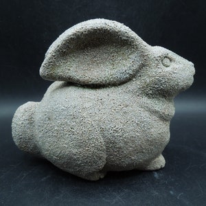 May include: A textured, gray rabbit sculpture with prominent ears and a rounded body. The bunny is in a seated position, with a rough, speckled surface. The sculpture is a decorative item, likely for home decor.