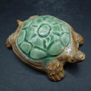 May include: A ceramic turtle figurine with a green glazed shell and brown body. The shell has a textured design and a glossy finish.