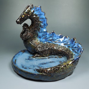 May include: A ceramic seahorse sculpture with a dark brown body and a vibrant blue mane and base. The sculpture has a textured surface and a glossy finish, creating a unique decorative piece.