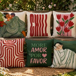 Può includere: Una collezione di cuscini decorativi con vari disegni. I cuscini presentano illustrazioni di una donna, tulipani e motivi astratti. Un cuscino ha la parola "CHILL" in rosso, e un altro dice "MORE AMOR POR FAVOR". I cuscini sono disposti su una panca di legno.