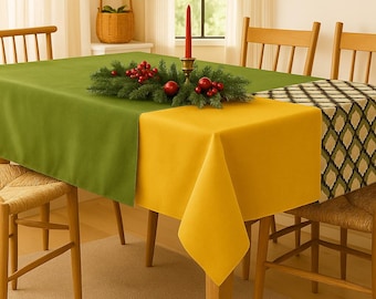 May include: A dining table set with a green and yellow tablecloth. A decorative centerpiece of greenery and red berries sits on the table, along with a red candle in a brass holder. Wicker chairs surround the table.