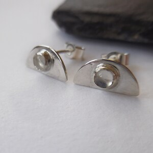 Peut inclure: Une paire de boucles d'oreilles en argent avec une forme de demi-lune et une pierre précieuse transparente au centre.