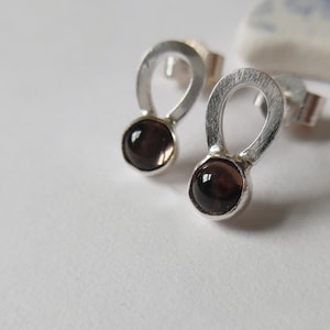 May include: A pair of silver earrings with a teardrop shape and a dark brown gemstone in the centre.
