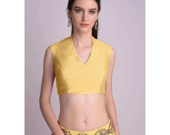 May include: A sleeveless, yellow crop top with a V-neck. The top is made of a textured fabric. The image also shows a matching yellow skirt with decorative beading at the waist. The text "Daivee Creation" is in the upper right corner.