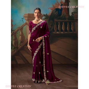 May include: A woman wearing a deep purple velvet sari with intricate gold and silver embroidery. The sari features a matching blouse with short sleeves and a detailed border. The background includes a painted mural with a peacock.