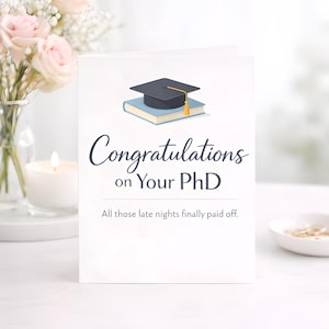 Puede incluir: Tarjeta de graduación blanca con el texto "Congratulations on Your PhD" en fuente cursiva. La tarjeta presenta una ilustración de un birrete sobre un libro. También se incluye el texto "All those late nights finally paid off".