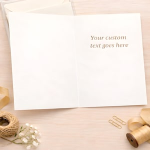 May include: A blank greeting card with the text "Your custom text goes here" printed in brown. The card is open on a light wood surface, with a clear plastic case, a spool of twine, paper clips, and decorative ribbon.