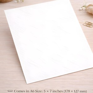 May include: A white A6 card, measuring 5 x 7 inches (178 x 127 mm), with a subtle textured pattern. The card is printed on premium 300gsm cardstock. The image shows the card at an angle, with a wooden surface in the background.
