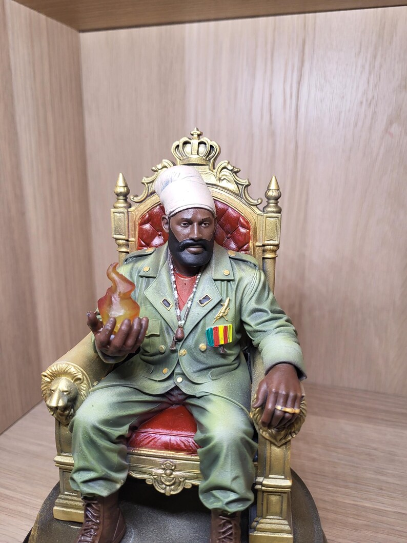 May include: A detailed figurine of a bearded individual wearing a light-coloured turban and a green military-style jacket, seated on an ornate gold throne with red upholstery. The figure holds a translucent orange flame and wears a gold ring.