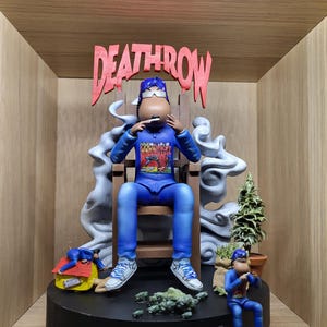 Könnte beinhalten: Blaue Figur einer Person, die auf einem Holzstuhl sitzt und raucht. Die Figur trägt einen blauen Trainingsanzug und weiße Turnschuhe. Auf dem Sockel steht "RECORDS" und oben "DEATHROW". Es gibt zwei kleinere Figuren und einen kleinen Baum.