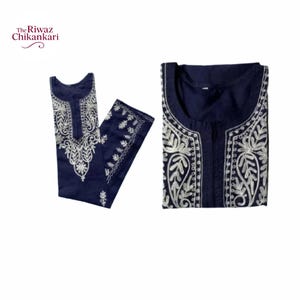 Puede incluir: Conjunto de túnica y pantalón bordados en azul marino. La túnica y el pantalón están doblados y se muestran sobre un fondo blanco. La túnica presenta un intrincado bordado floral blanco alrededor del escote y en la parte delantera. La marca "The Riwaz Chikankari" está en la esquina superior izquierda.