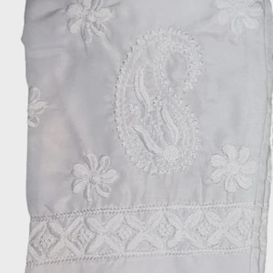 Puede incluir: Tejido blanco con intrincados bordados florales y de cachemira. El dise&ntilde;o presenta costuras detalladas, incluyendo flores y un motivo central de cachemira. La tela est&aacute; doblada, mostrando el delicado trabajo de bordado.