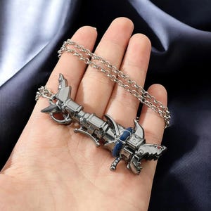 May include: A silver-colored shark pendant necklace. The shark pendant has a mechanical design with blue and red accents. The necklace is displayed on a hand against a dark blue background.