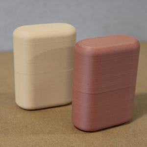 May include: Two rectangular, rounded-top containers. One is a light beige color, and the other is a muted reddish-brown. Both have a smooth, matte finish. The containers are side-by-side, suggesting a set or pair of storage items.