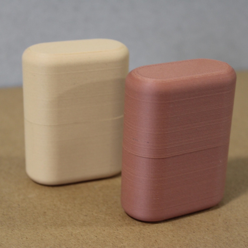 May include: Two rectangular, rounded-top containers. One is a light beige color, and the other is a muted reddish-brown. Both have a smooth, matte finish. The containers are side-by-side, suggesting a set or pair of storage items.