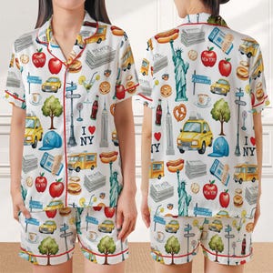 Puede incluir: Conjunto de pijama blanco con estampado tem&aacute;tico de la ciudad de Nueva York. La camiseta de manga corta y los pantalones cortos presentan im&aacute;genes ic&oacute;nicas de la ciudad como la Estatua de la Libertad, taxis amarillos y manzanas. Ribete rojo.