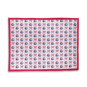 May include: A rectangular white fabric with a repeating pattern of blue, round-shaped objects with pink bows. The fabric has a bright pink border.