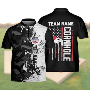 Op de afbeelding: Zwart-wit cornhole poloshirt met een grafisch ontwerp. De voorkant heeft een cornhole logo, de tekst "YOUR NAME" en een patroon van cornhole boards. De achterkant heeft de tekst "TEAM NAME" en "CORNHOLE" met een Amerikaans vlagontwerp.