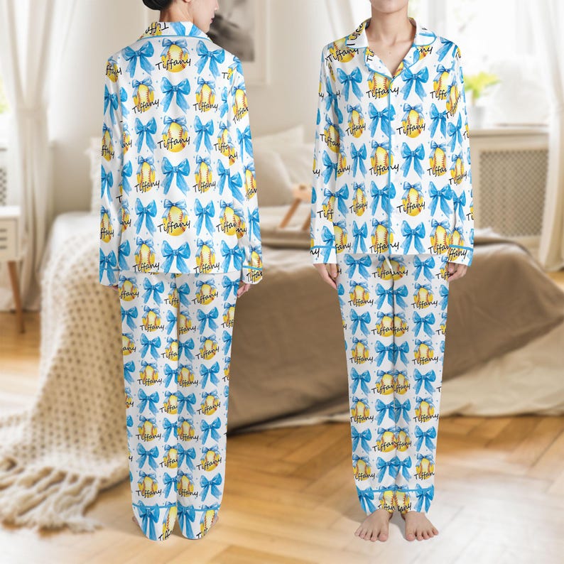 以下が含まれることがあります： 白いパジャマセット。青いリボン、黄色の野球ボール、そして「Tiffany」の文字が繰り返されるパターン。長袖トップスは襟付き、パンツはウエストに紐付き。柔らかく軽い生地で作られています。