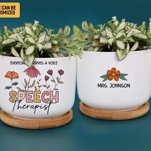 Puede incluir: Dos macetas de cerámica blanca con diseños florales y el texto "SPEECH Therapist" y "MRS. JOHNSON". Cada maceta se asienta sobre un platillo redondo de madera y contiene una planta verde. La esquina superior izquierda tiene el texto "NAME CAN BE CUSTOMIZED".