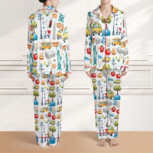 Puede incluir: Conjunto de pijama blanco con un estampado colorido con tem&aacute;tica de la ciudad de Nueva York. La parte superior de manga larga y los pantalones presentan monumentos ic&oacute;nicos, alimentos y el texto "I NY". El ribete rojo acent&uacute;a los bordes del pijama.