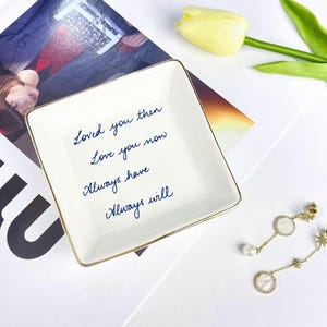Może przedstawiać: Kwadratowa, biała ceramiczna patera z pozłacaną obwódką i niebieskim, pisanym tekstem, który brzmi: "Loved you then, Love you now, Always have, Always will". Widoczna jest również para złotych kolczyków z perłowymi i gwiazdkowymi akcentami.
