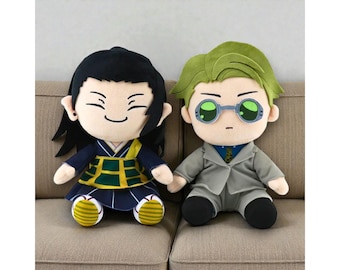 May include: Two plush dolls of anime characters are seated on a couch. One doll has black hair and a smiling face, wearing a blue and yellow outfit. The other doll has green hair, glasses, and a gray suit. They are holding hands.