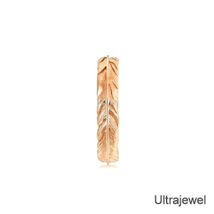 May include: A gold-coloured ring with a feather design. The ring has a warm, metallic tone and features detailed feather imprints along its surface. The ring is set against a white background.