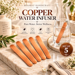 May include: A set of five flat, rectangular copper water infuser sticks with rounded ends. One stick is submerged in a clear glass carafe filled with water, while four identical copper sticks are arranged in a row on a marble surface.