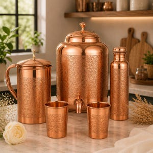 Può includere: Un set di utensili da cucina in rame composto da un grande distributore d'acqua con rubinetto, una brocca con manico, due bicchieri e una bottiglia d'acqua alta. Ogni pezzo è realizzato in rame lucido con un complesso motivo floreale in rilievo.