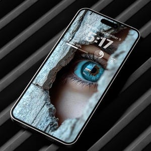 May include: A smartphone displays a close-up of a blue eye with a textured background. The screen shows the time as 5:17 and the date as Monday, September 6. The phone has a silver frame and is angled on a black, ridged surface.