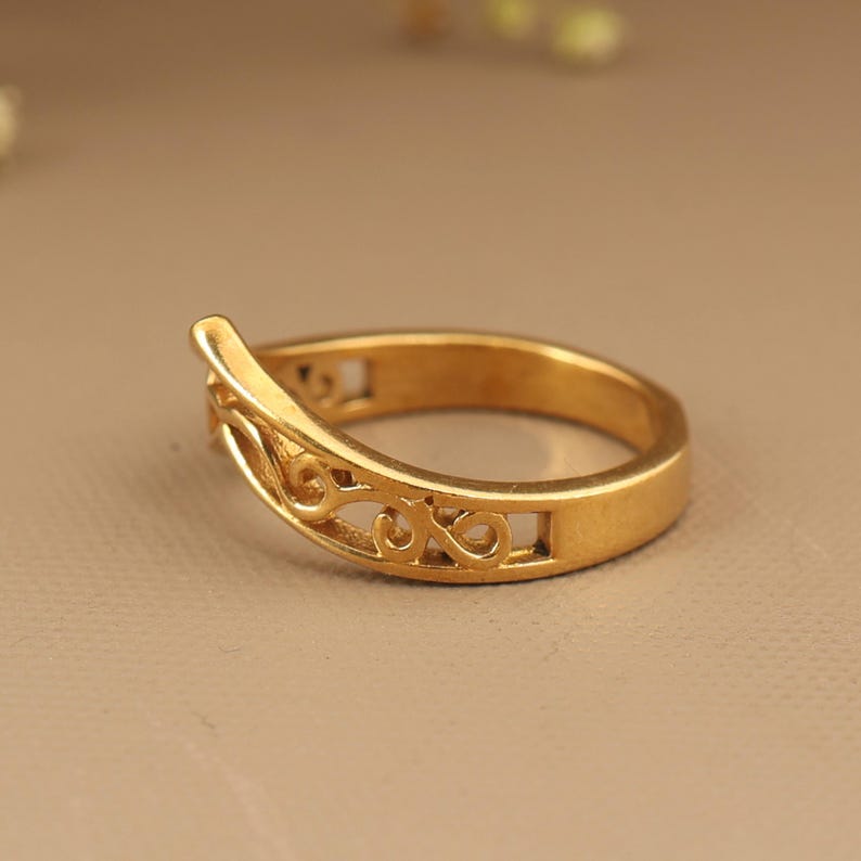 May include: A gold-colored ring with an openwork design. The ring features a curved, raised section and intricate scrollwork along the band. The ring is a size 7.