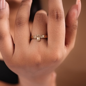 May include: A gold ring with an owl motif. The ring has a detailed owl figure at the centre, with wings extending on either side. The ring is worn on a finger, showcasing the intricate details of the jewellery.