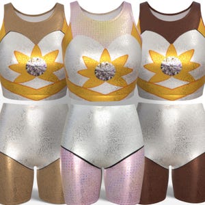 Peut inclure: Trois ensembles de vêtements de sport assortis. Chaque ensemble comprend un crop top et un short. Les hauts sont métalliques avec un motif floral et une grosse gemme au centre. Les shorts sont métalliques avec une couleur contrastante sur la partie inférieure.