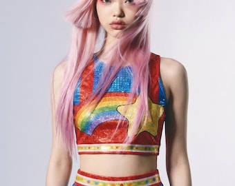 May include: A two-piece outfit consisting of a sleeveless, red, blue, and yellow cropped top featuring a rainbow and star graphic, paired with a matching blue, red, and silver metallic skirt with a textured, shimmering finish throughout.