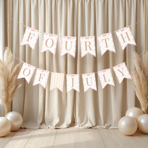 May include: A banner with the words "FOURTH OF JULY" in a light brown font, strung across a neutral-toned background. The banner flags are white with a scalloped edge and a light brown border. Decorative elements include balloons and pampas grass.
