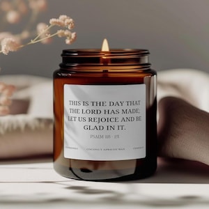 Puede incluir: Una vela encendida en un tarro de cristal marrón con una etiqueta blanca. La etiqueta dice: "THIS IS THE DAY THAT THE LORD HAS MADE; LET US REJOICE AND BE GLAD IN IT. PSALM 118:24". La vela está hecha con cera de coco y albaricoque.