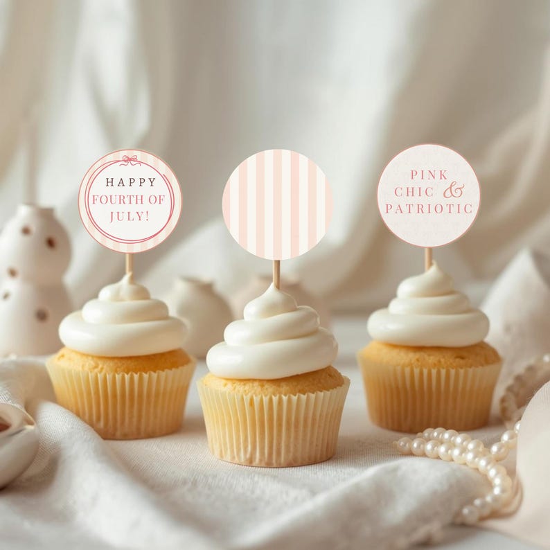 May include: Three cupcakes with white frosting and decorative toppers. One topper reads "Happy Fourth of July!" in a circular design. Another has pink stripes, and the third says "Pink Chic & Patriotic."