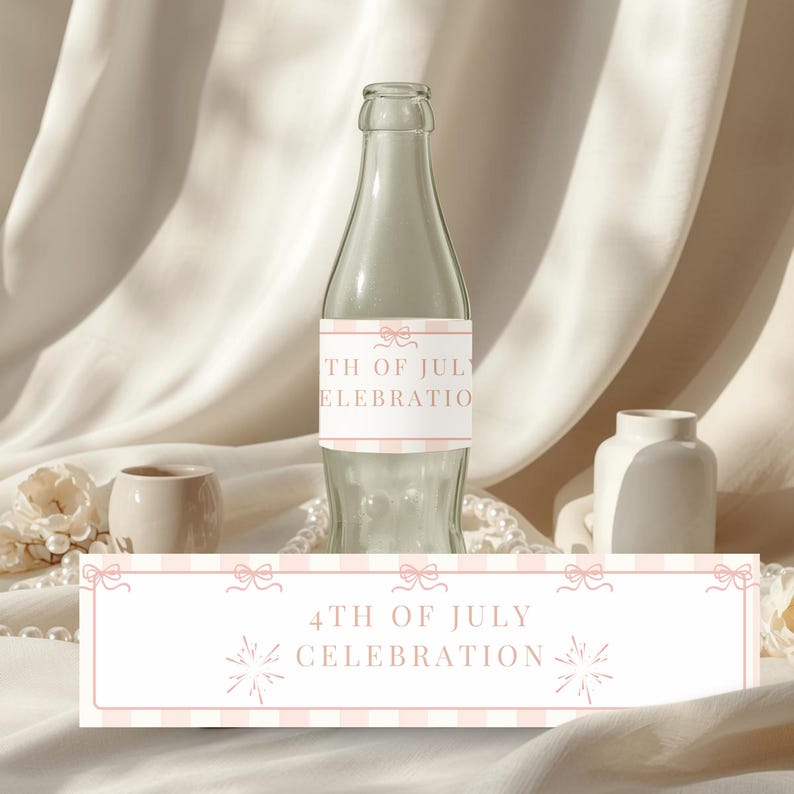 May include: A clear glass bottle with a label that reads "4th of July Celebration." The label has a pink and white striped pattern with bow accents. The bottle is surrounded by decorative elements, including a small vase and pearls.