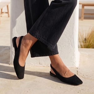 May include: A pair of black suede slingback flats with a square toe design and a thin heel strap. The shoes feature a low profile, a smooth matte finish, and a minimalist construction that leaves the heel exposed while covering the front of the foot.