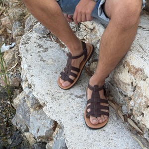 Pu&ograve; includere: Sandali in pelle marrone con design a cinturini intrecciati. I sandali hanno una suola marrone chiaro e un cinturino alla caviglia. Adatti per attivit&agrave; all'aperto e occasioni informali.