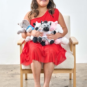 May include: A person seated in a wooden chair, wearing a red dress and white shoes, holding several stuffed animal toys. The toys include a gray elephant, a zebra, a cow, and a pink pig. The background is a plain white wall.