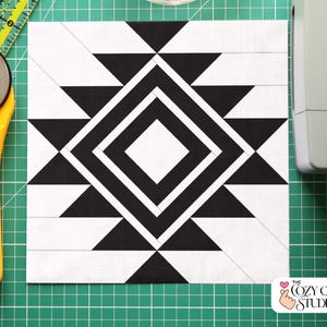 May include: A black and white geometric quilt block with a diamond and triangle design. The quilt block is on a green cutting mat with a yellow rotary cutter and ruler.