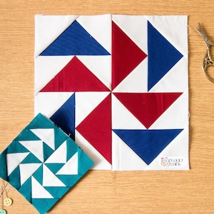 May include: Two quilt blocks with red, white, and blue triangular patterns. One block is a larger square with a pinwheel design, and the other is a smaller square with a similar pattern. A pair of scissors rests on a wooden surface.