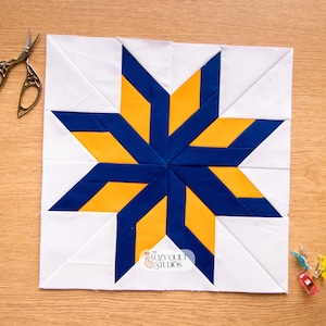 Peut inclure: Un bloc de patchwork fait à la main avec un motif d'étoile bleu et jaune sur fond blanc. Le bloc carré présente un motif géométrique. Une paire de ciseaux et des pinces à couture sont placés près du bloc. Le logo Cozy Quilt Studios est visible.
