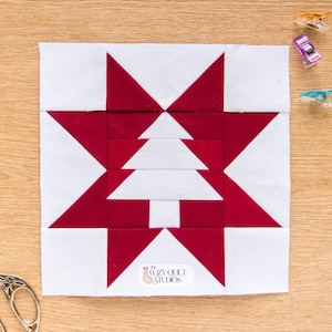 Può includere: Un blocco per trapunta quadrato caratterizzato da una grande stella rossa con una forma di albero di Natale bianco al centro. Il design è composto da pezzi di tessuto rossi e bianchi. È attaccata una piccola etichetta bianca con il testo The Cozy Quilt Studios.