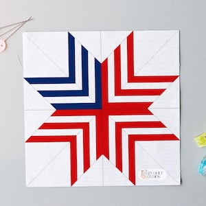 May include: A square quilt block featuring a star design in red, white, and blue. The star is made of red and blue stripes on a white background. Sewing pins and clips are also visible.