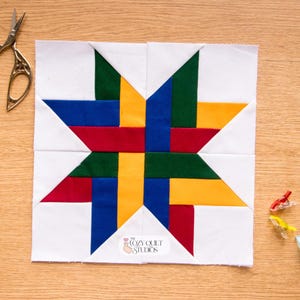 May include: A colorful quilt block with a star design, featuring red, blue, green, and yellow fabric on a white background. Gold scissors and quilting clips are placed on a wooden surface near the block. The Cozy Quilt Studios logo is visible.