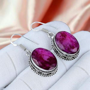 Peut inclure: Une paire de boucles d'oreilles en argent avec de grandes pierres précieuses magenta de forme ovale. Les pierres sont serties dans des montures en argent ornées et détaillées avec une bordure décorative. Fermeture à crochet.