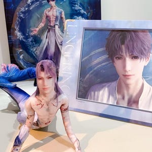 Peut inclure: Une présentation comprenant un portrait encadré d'un homme aux cheveux violets, une figurine imprimée en 3D et une affiche. La figurine est un personnage masculin aux cheveux violets et au torse nu. L'affiche et le portrait encadré présentent des œuvres d'art similaires.